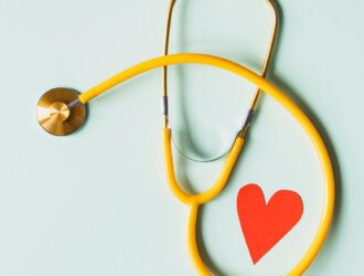 medical stethoscope with red paper heart on white surface